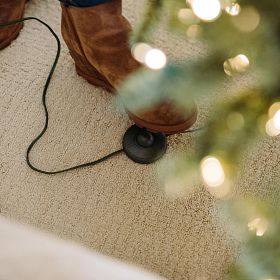 Woman wearing brown boots stepping on foot pedal of artificial Christmas tree