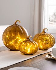 Trio of lit glass pumpkins on a dining table