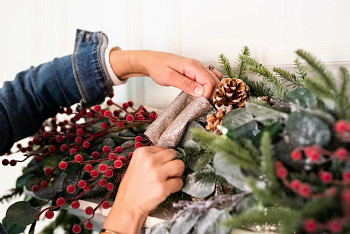 Hands attaching a champagne scalloped tree ribbon to a Christmas garland