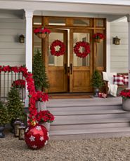 Porch décor idea with red Christmas wreaths, garlands, and hanging baskets