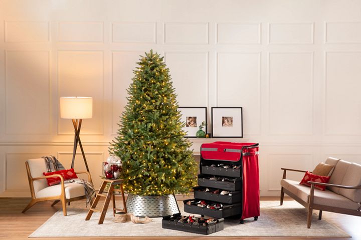 Pre-lit Christmas tree next to a red ornament storage chest in the living room
