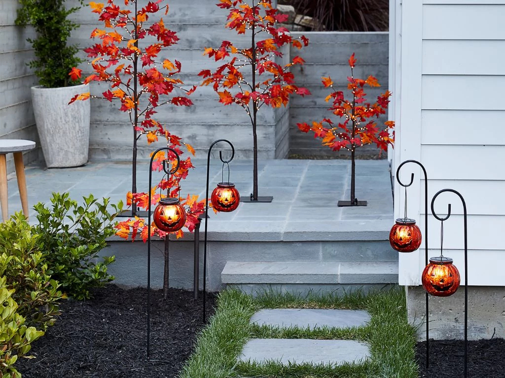Solar-powered Jack-o’-lantern pathway lights and artificial maple trees displayed outdoors