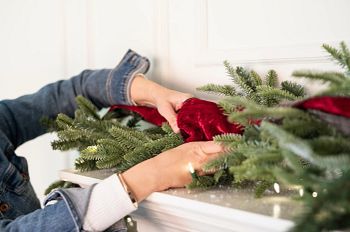 Hands adding red ribbon to artificial garland