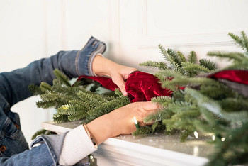 Hands decorating a Christmas garland with red velvet ribbon