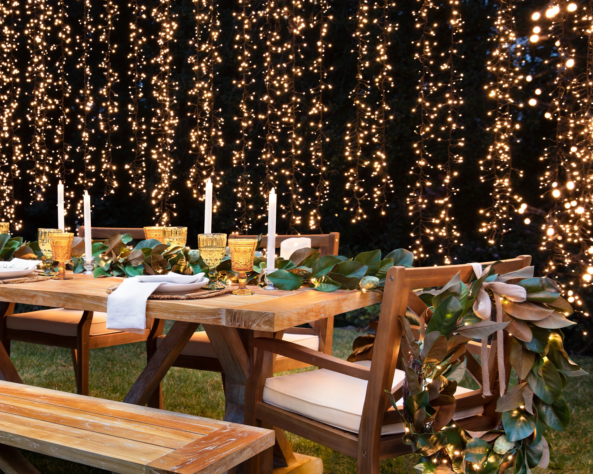 Outdoor dining table setup with magnolia leaf foliage and string lights