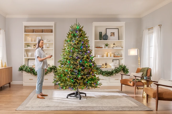 Une personne pointant une télécommande vers un sapin de Noël illuminé