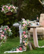 Outdoor wedding table decorated with artificial rose garland, champagne bottles and glasses, and serveware