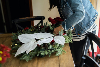 Hands decorating a Christmas wreath with oversized white magnolia picks