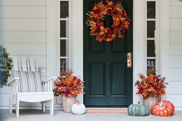 Porch decorated with autumn wreath, potted plants, and pumpkins