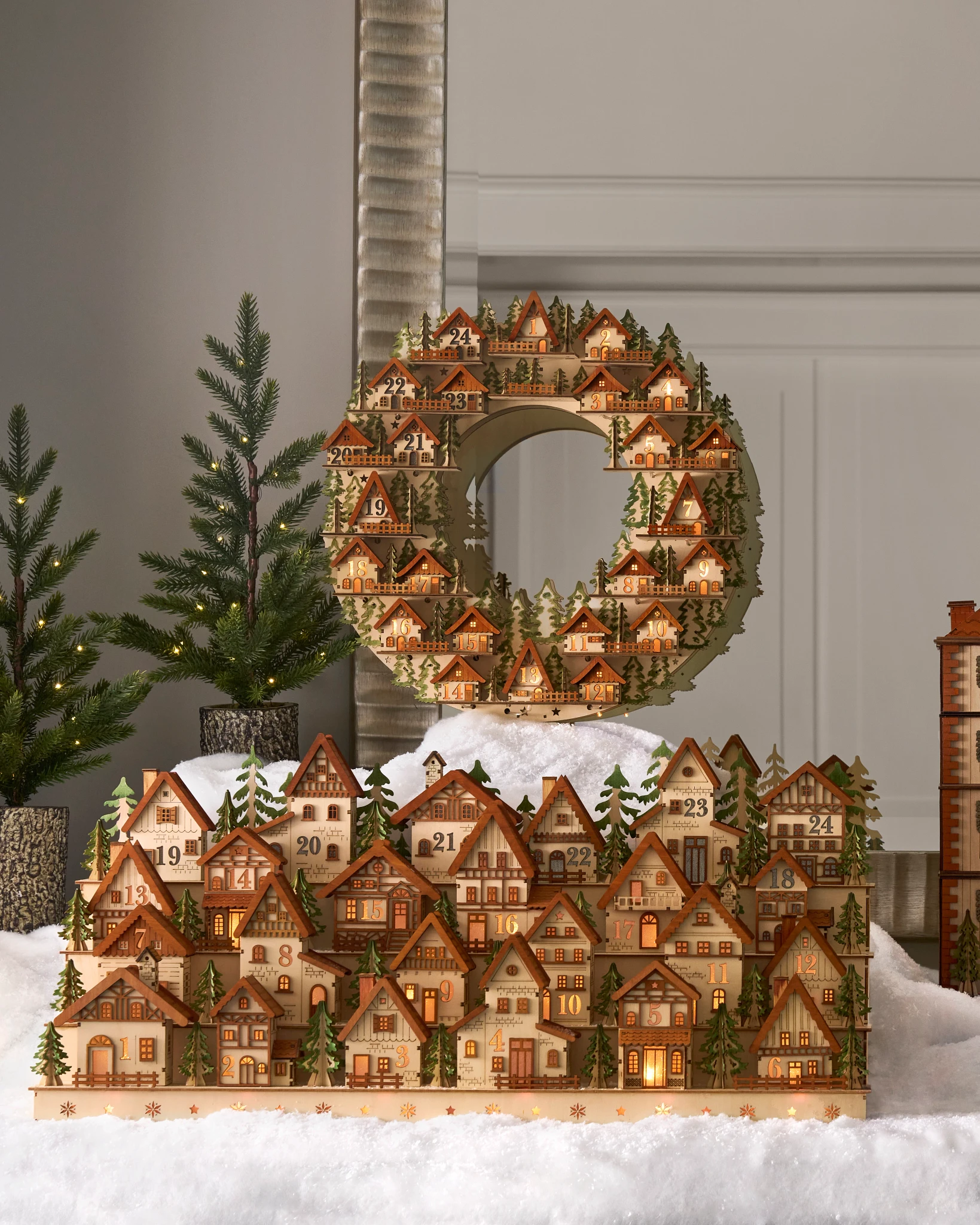 A festive advent calendar featuring charming illuminated houses, set in a snowy landscape with evergreen accents.