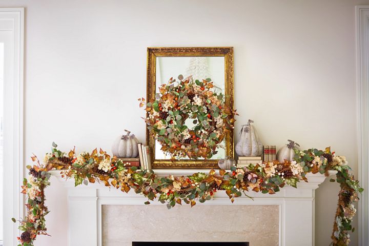 White mantel decorated with a gilded mirror, fall foliage, and white pumpkins