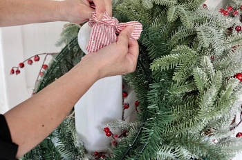 Hands tying red pinstriped ribbon to an artificial Christmas wreath
