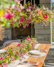 Outdoor dining table decorated with artificial spring flower garlands, white runner, and place settings