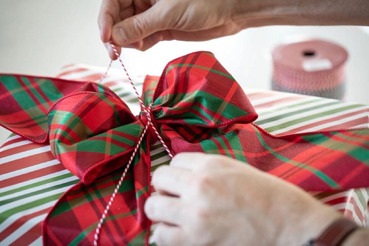 Pair of hands tying a red and green plaid ribbon onto a wrapped Christmas gift