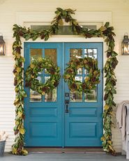 A blue front door decorated with wreaths and garlands
