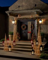 A porch decorated with Christmas greenery, lanterns, and wire cone trees