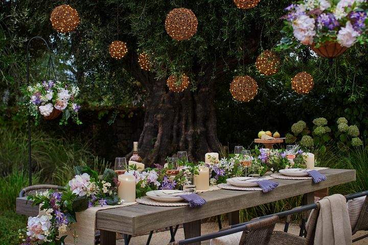 Outdoor dining area decorated with hanging lanterns, artificial floral garlands, flameless candles, and place settings