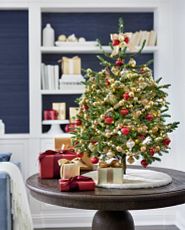 Tabletop artificial Christmas tree decorated with red and gold ornaments and ivory tree skirt