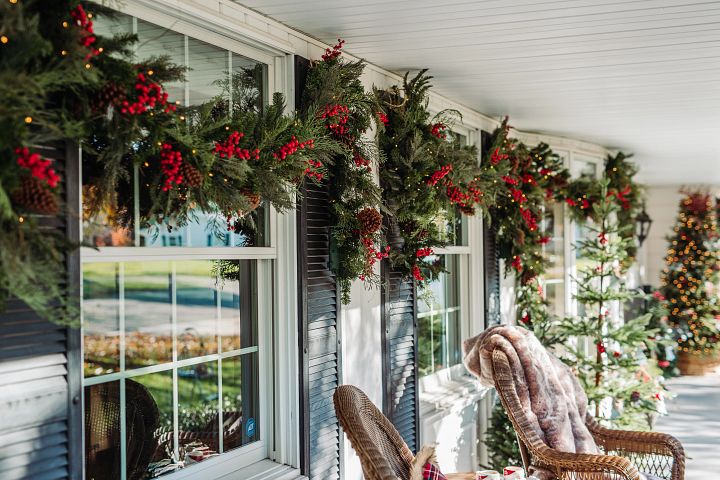 Front porch windows decorated with artificial Christmas greenery with berries and pinecones
