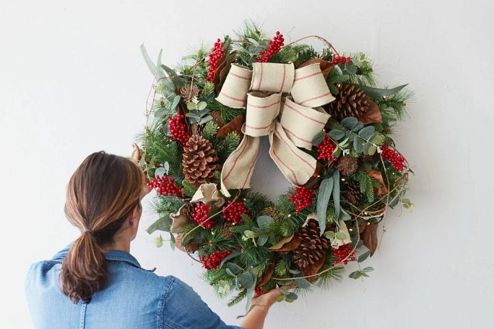Woman hanging an artificial Christmas wreath on a wall