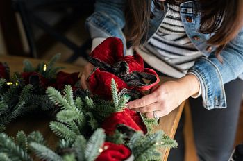 Hands tying ribbon to artificial Christmas wreath