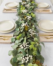Dining table with white tablecloth, place settings, and artificial garland centerpiece featuring seeded, silver dollar, willow eucalyptus leaves, and ivory berries