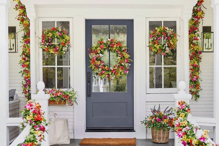 Alt text: Colorful artificial wreaths, garlands, and potted foliage on a porch