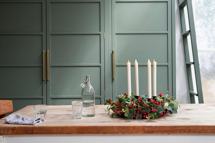 Rustic tabletop decorated with a Christmas wreath with candles and holly
