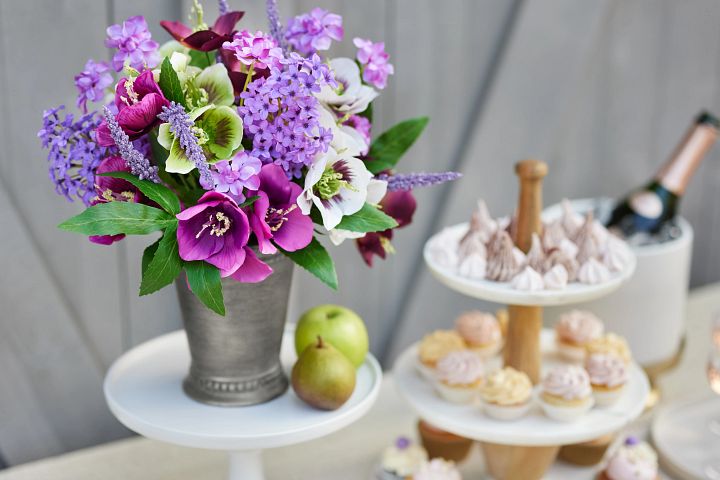 Purple and white artificial flowers in a silver vase on a brunch buffet table