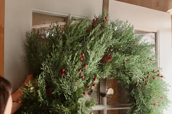 Woman hanging an artificial Christmas wreath from a metal hanger on the door