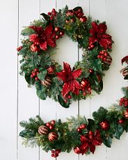Artificial Christmas wreath and garland decorated with poinsettias, berries, and ornaments on white bakcground