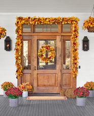 Front porch decorated with artificial fall wreath, garland, hanging basket, floral arrangement, and potted mums