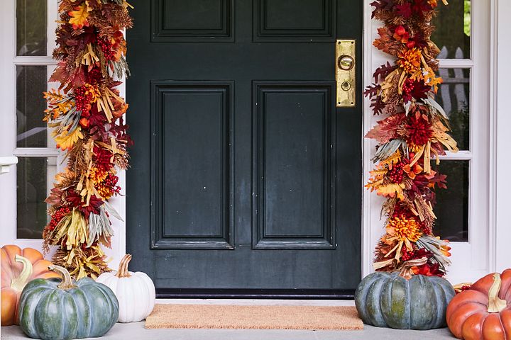 Black front door decorated with fall harvest foliage and artificial pumpkins