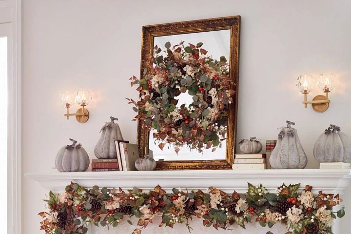 White mantel decorated with gilded mirror, artificial fall wreath and garland, white faux pumpkins, and books