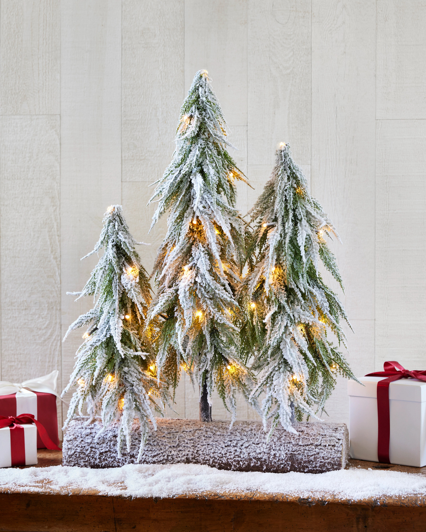 Artificial tabletop mini trees with faux snow on a console table