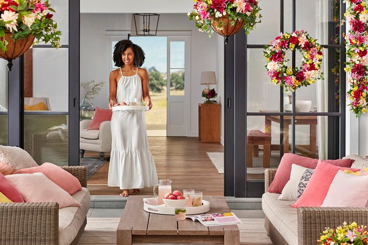 Woman holding tray walking into a porch decorated with artificial flowers