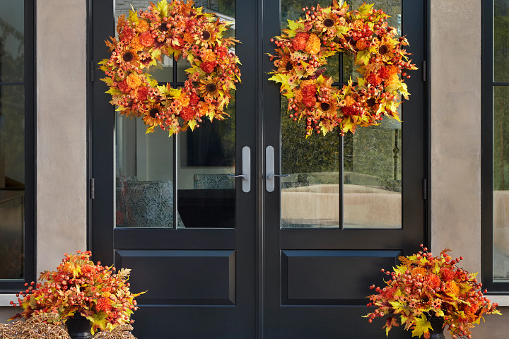 Two doors decorated with colorful autumn wreaths and urn fillers
