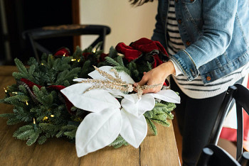 Hands decorating a Christmas wreath with metallic plume beaded branch picks