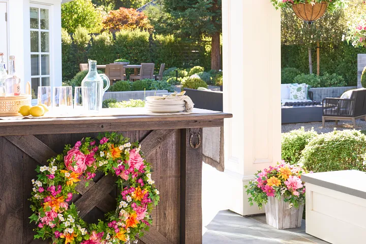Patio with outdoor bar decorated with colorful flower wreath, potted foliage, and tableware