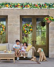 Children sitting on outdoor couch on the patio decorated with artificial flower wreaths, garlands, and hanging baskets