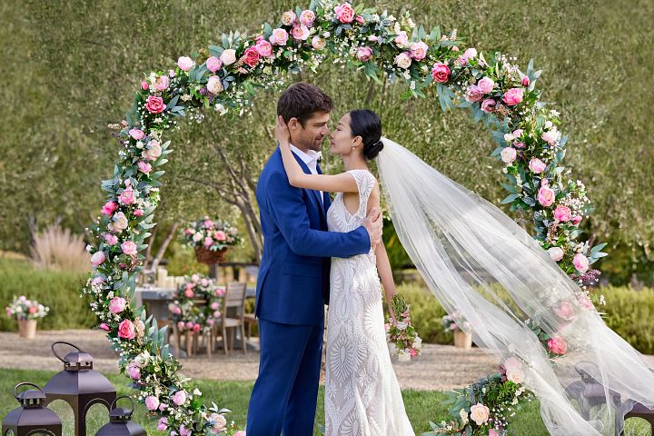 Outdoor wedding couple posing in front of a ceremonial backdrop made of spring flowers