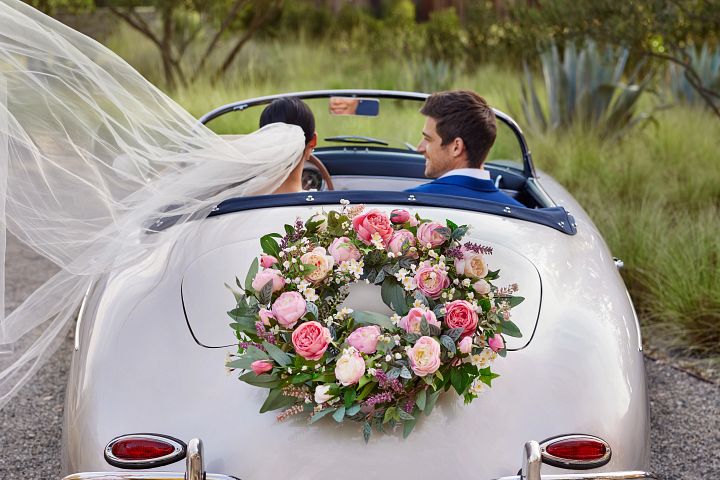 Newlyweds in a convertible car decorated with a flower wreath