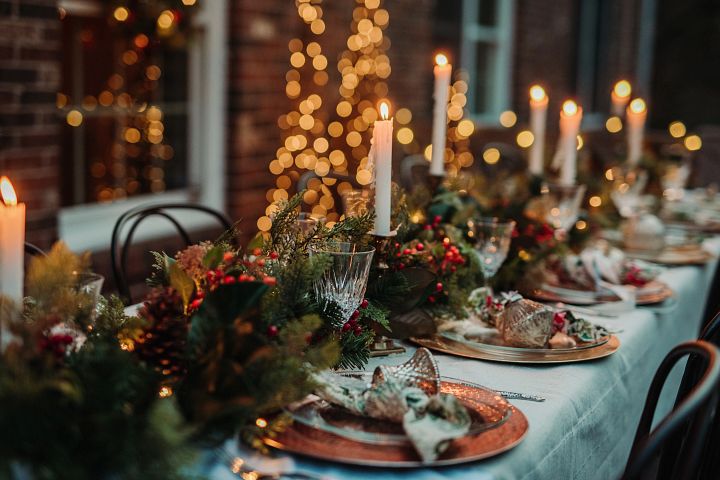 Outdoor dining table decorated with artificial greenery, candles, and place settings