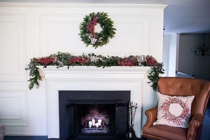 A fireplace mantel decorated with a wreath and garland in a classic Christmas decorating theme