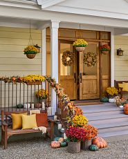 Front porch decorated with artificial fall greenery and wooden bench with pillows and throw blanket