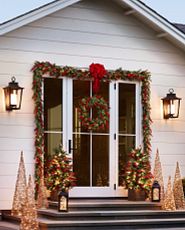 Porte vitrée décorée avec des décorations végétales, des lanternes et des sapins illuminés.