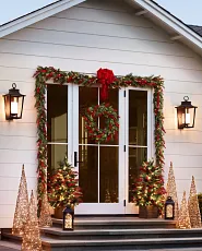 Glass door décor with greenery, lanterns, and lit accent trees