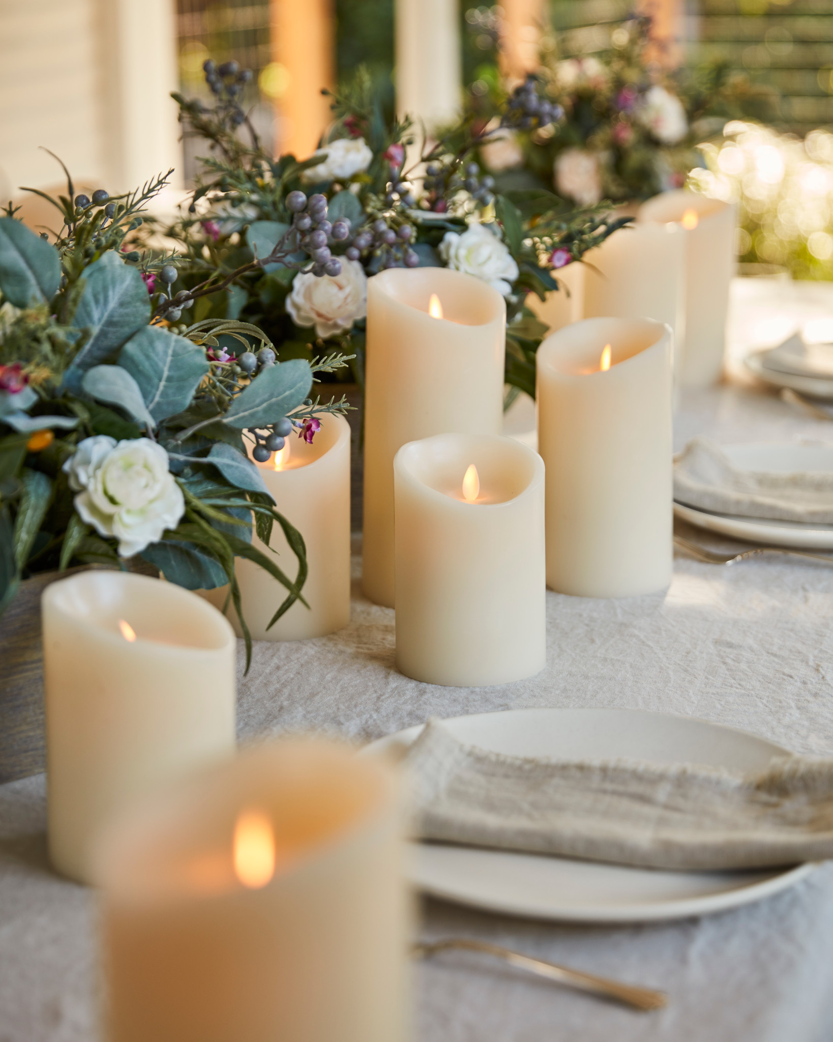 Outdoor dining table decorated with faux candles, artificial spring garland, taupe tablecloth, plates, and napkins