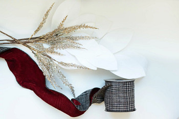 Flatlay of wreath decorations such as magnolia branch picks, red velvet ribbon, and metallic plume branch picks