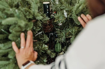 Person moving tree branches away from artificial Christmas tree trunk